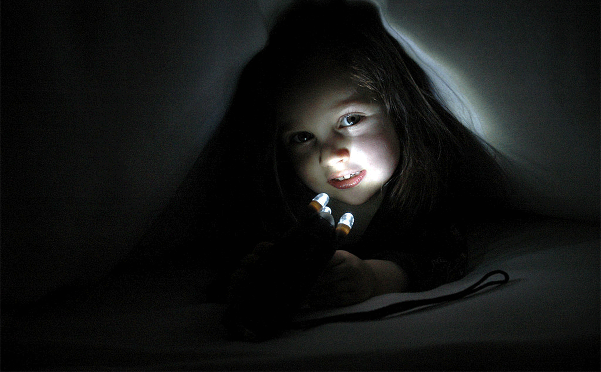 طفلة تحمل مصباحاً داخل فراشها 