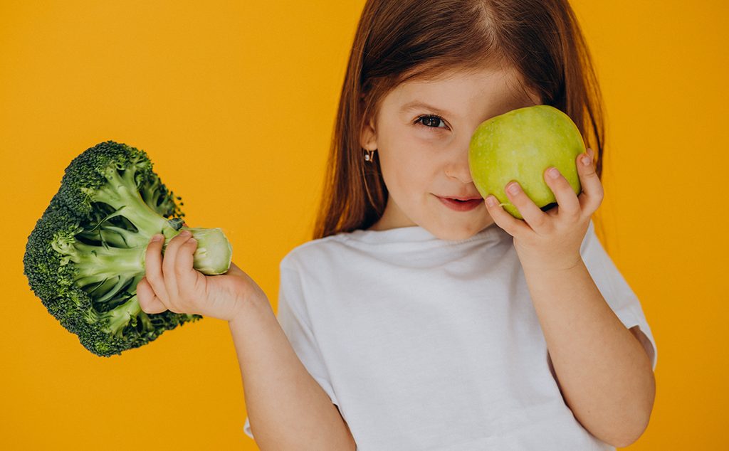 طفلة صغيرة تحمل تفاحة وبروكولي