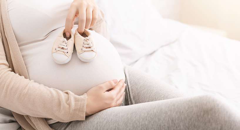 حامل تضع حذاء طفلها الذي لم يولد بعد على بطنها