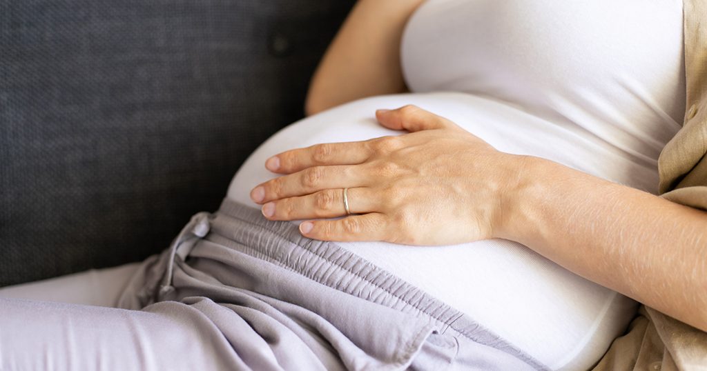 حامل تضع يدها على بطنها لتشعر بحركة الجنين