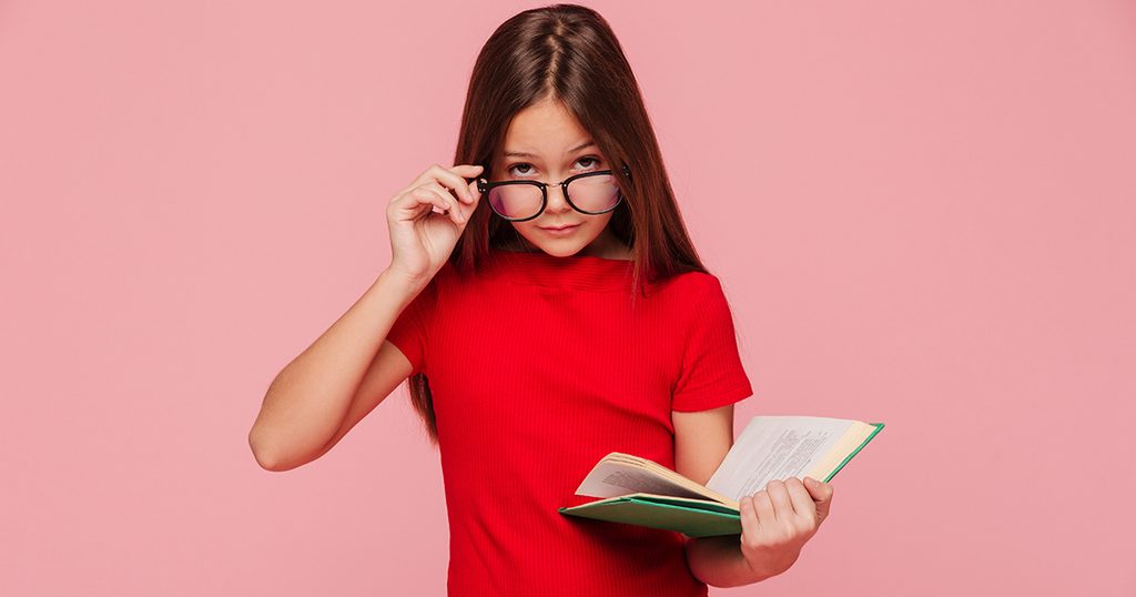 فتاة تُمسك بنظّاراتها وتحكل كتابًا في يدها