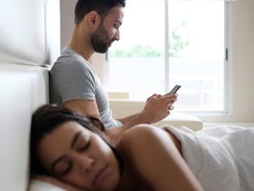 زوج يتحدث بالسر على هاتفه خلال نوم زوجته