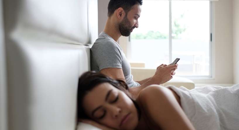 زوج يتحدث بالسر على هاتفه خلال نوم زوجته