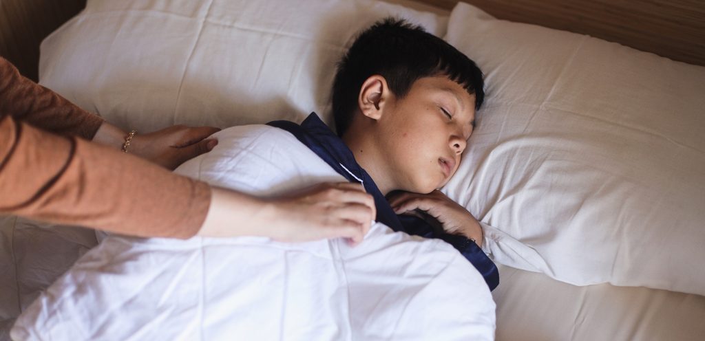 طفل نائم في سريره ووالدته تُغطّيه