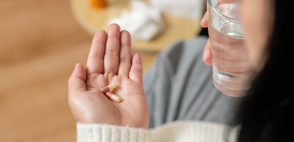 امرأة تُمسك حبّتين من الدواء في يدها وكوب من الماء في اليد الأخرى