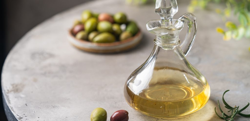 قارورة زجاجية من زيت الزيتون وخلفها حبوب من الزيتون