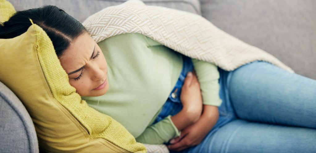 امرأة تُعاني من ألم البطن وتستلقي على الأريكة