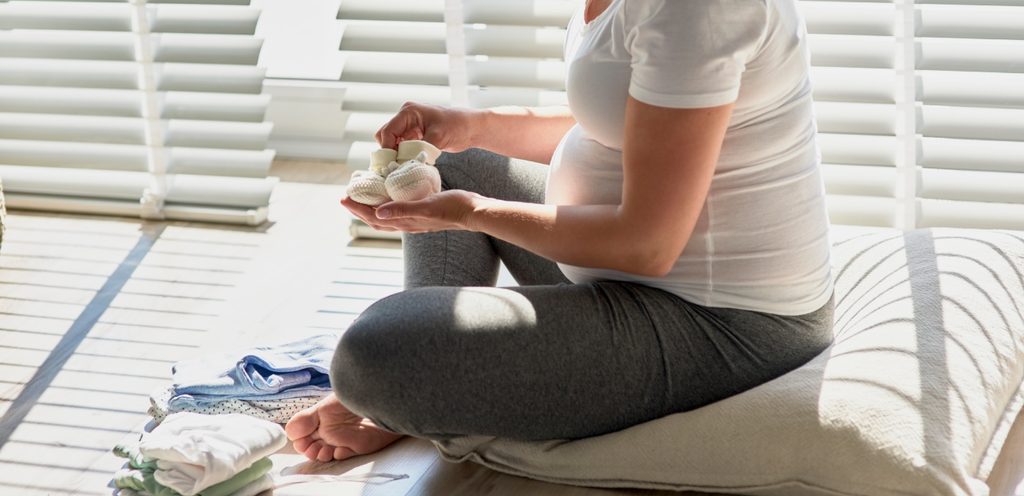 امرأة حامل تجلس على وسادة وتمسك بحذاء مولود جديد