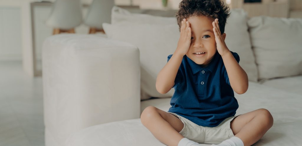 طفل سعيد يجلس على الكنبة ويضع يديه على وجهه