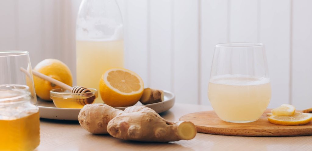 قطعة من الزنجبيل وخلفها أكواب من الليمون والعسل