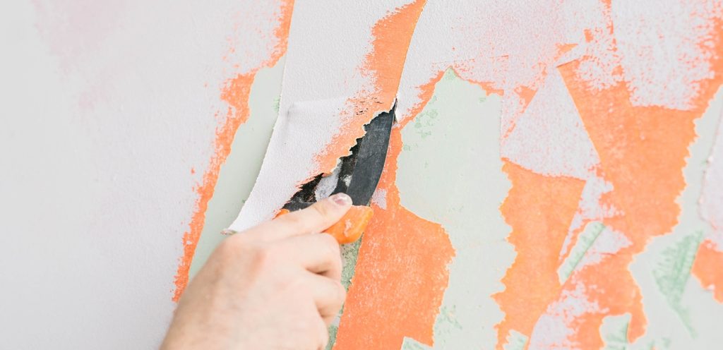 يد تُمسك أداة حادّة وتُحاول إزالة الدهان عن الحائط