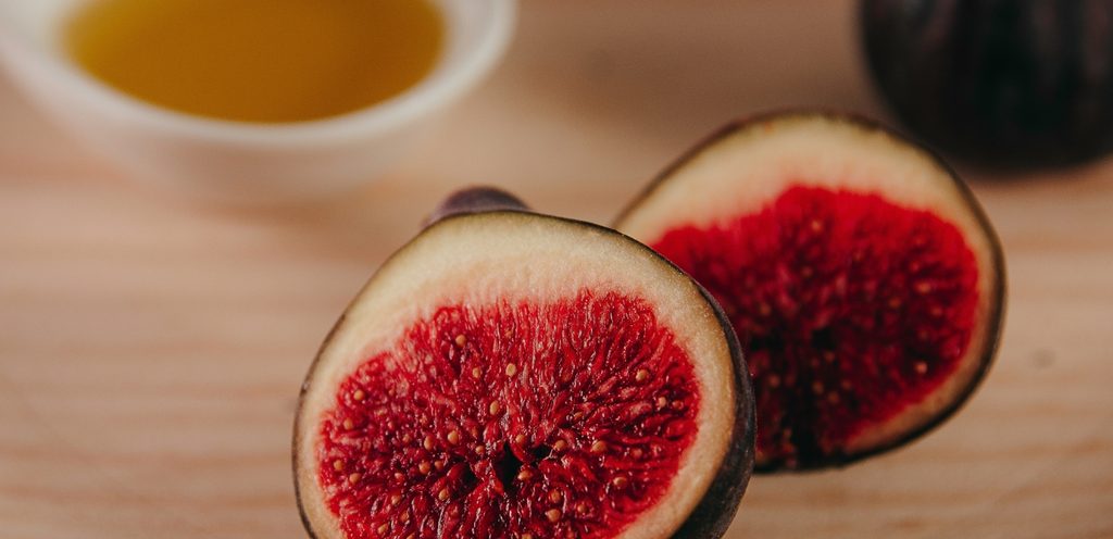 ثمرة تين مقطّعة إلى نصفين وزبدية من الزيت في الخلفيّة