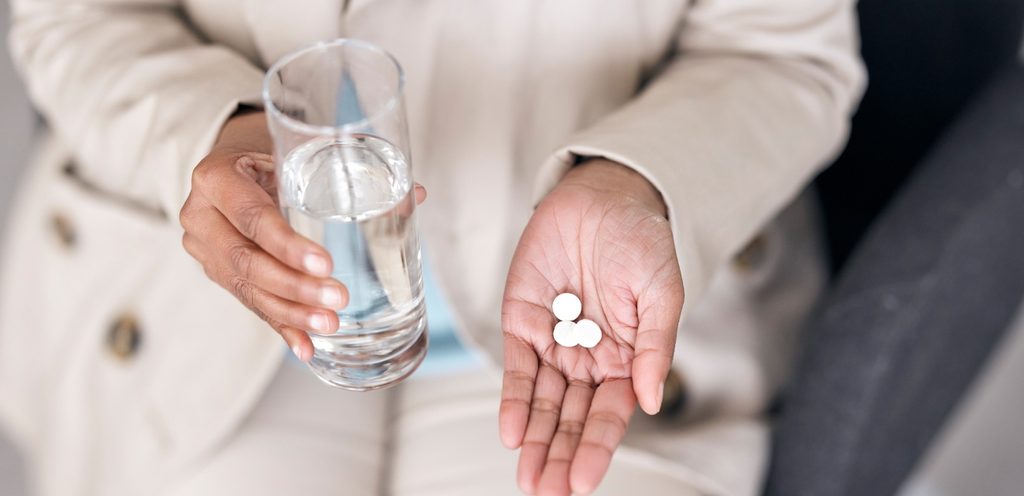 امرأة تُمسك في يديها كوب من الماء وحبوب دواء
