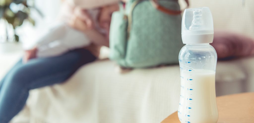 زجاجة من حليب الأطفال وأمّ مع رضيعها في الخلفيّة