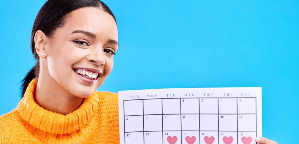 امرأة تبتسم وتحمل برنامج دورتها الشهريّة