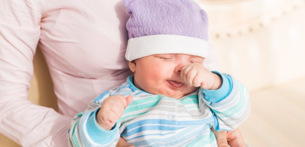 طفل رضيع يضع يده على أنفه وهو بحضن والدته