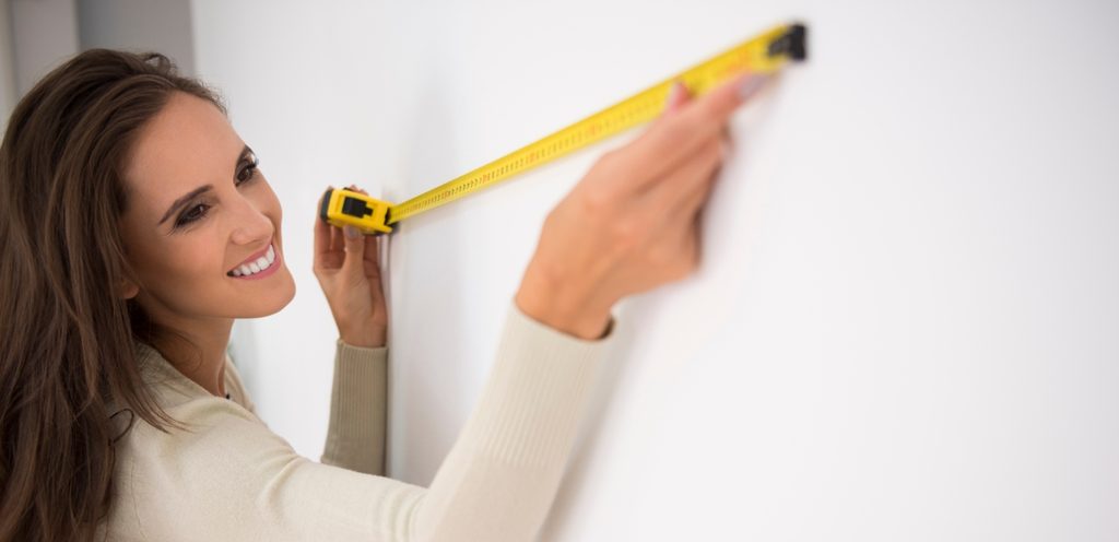 امرأة مُبتسمة وتقيس الحائط بالمقياس