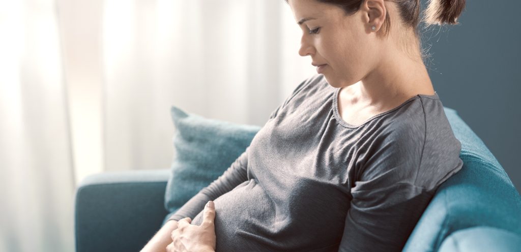 امرأة حامل تنظر إلى بطنها وتضع يدها عليه