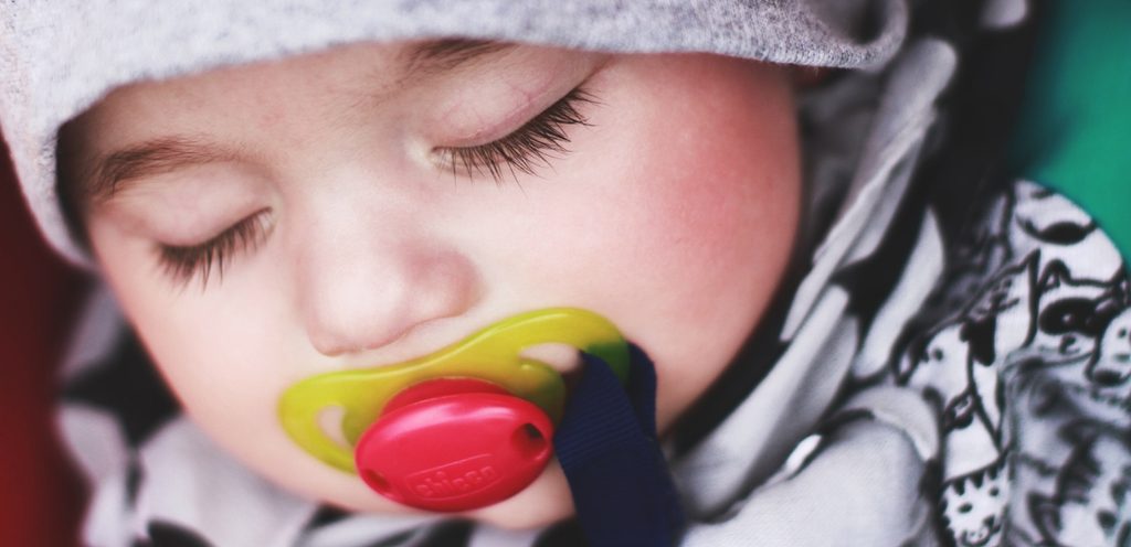 طفل رضيع نائم وفي فمه لهاية صفراء وحمراء