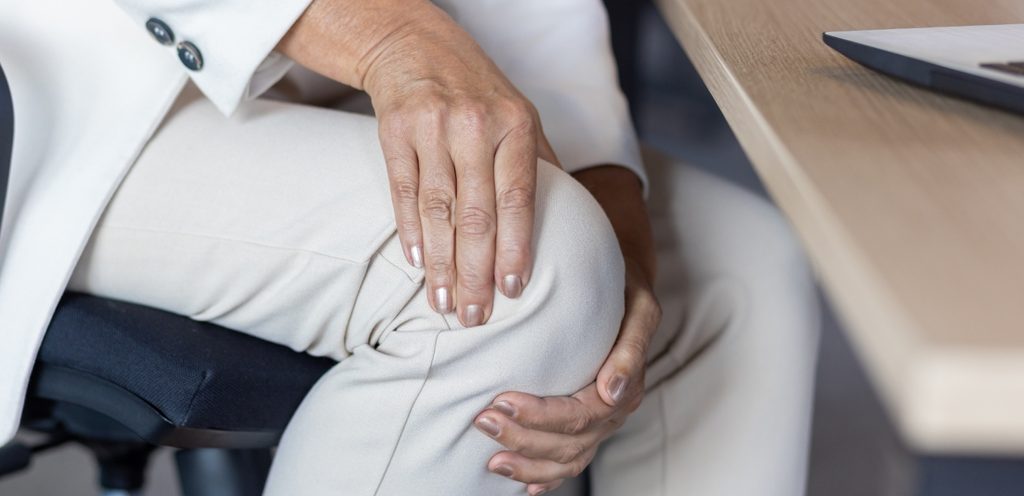 امرأة تضع يديها على ركبيتها وهي جالسة على الكرسي أمام مكتبها