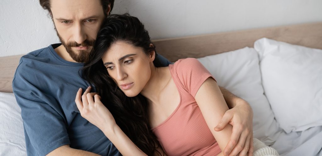 زوج يحضن زوجته على السرير وهما حزينان