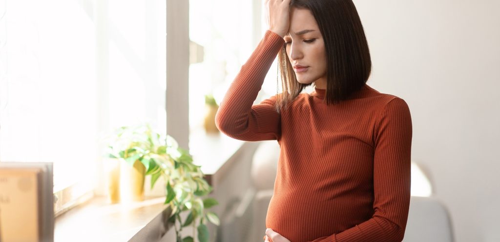 امرأة حامل منزعجة تضع يدًا على رأسها والأخرى على بطنها