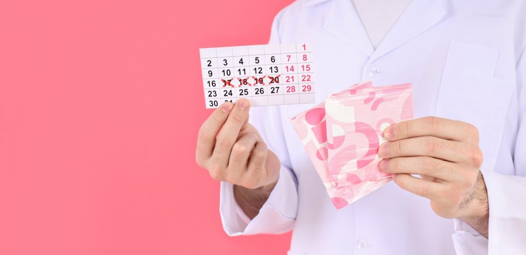 طبيب يمسك فوط نسائيّة صحيّة ورزنامة