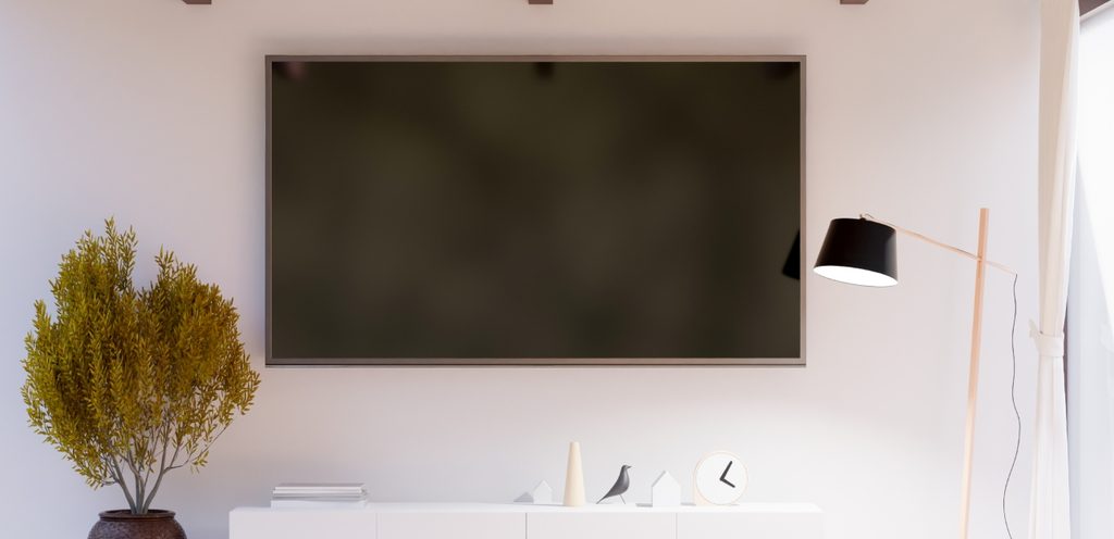 تلفاز معلّق على حائط أبيض وبجانبه ضوء ونبتة