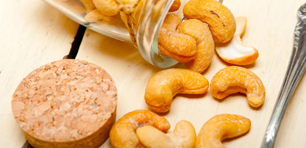 مرطبان من الزجاج مفتوح وينزل منه حبوب الكاجو على الطاولة