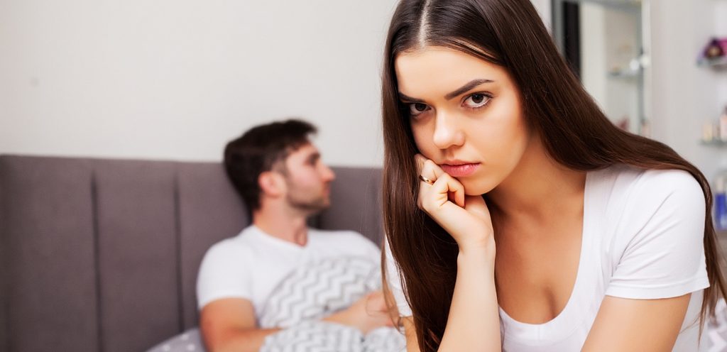 امرأة غاضبة وخلفها زوجها يجلس في السرير
