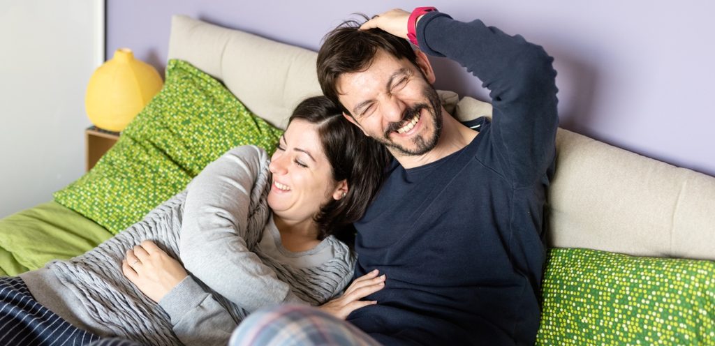 زوجان يجلسان إلى جانب بعضهما البعض على السرير وهما يضحكان