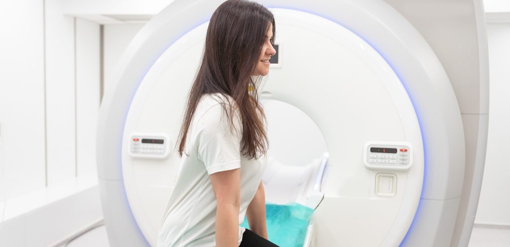 امرأة تجلس مبتسمة أمام آلة الأشعّة المقطعيّة