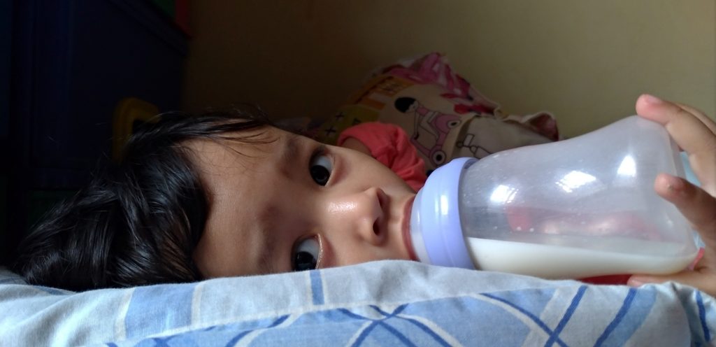 طفل رضيع يشرب زجاجة من الحليب وينظر لأعلى