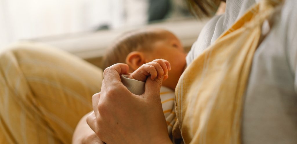 أمّ تمسك يد طفلها أثناء رضاعته منها