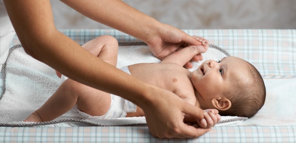 أمّ تمسك يدي طفلها الرضيع الذي يستلقي وهو يبتسم