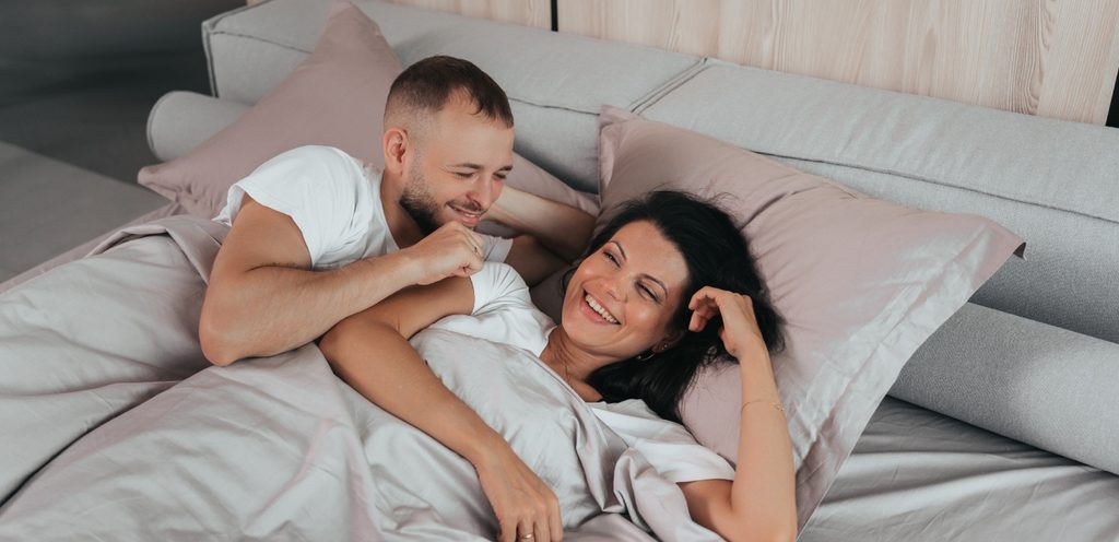 زوج يقترب من زوجته على الفراش وهما يضحكان