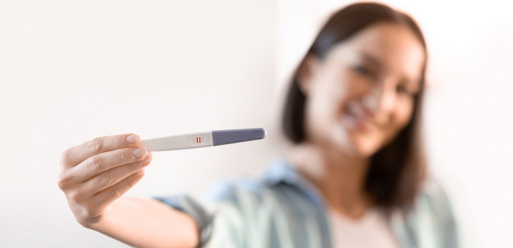 امرأة تُمسك اختبار حمل وهي مبتسمة