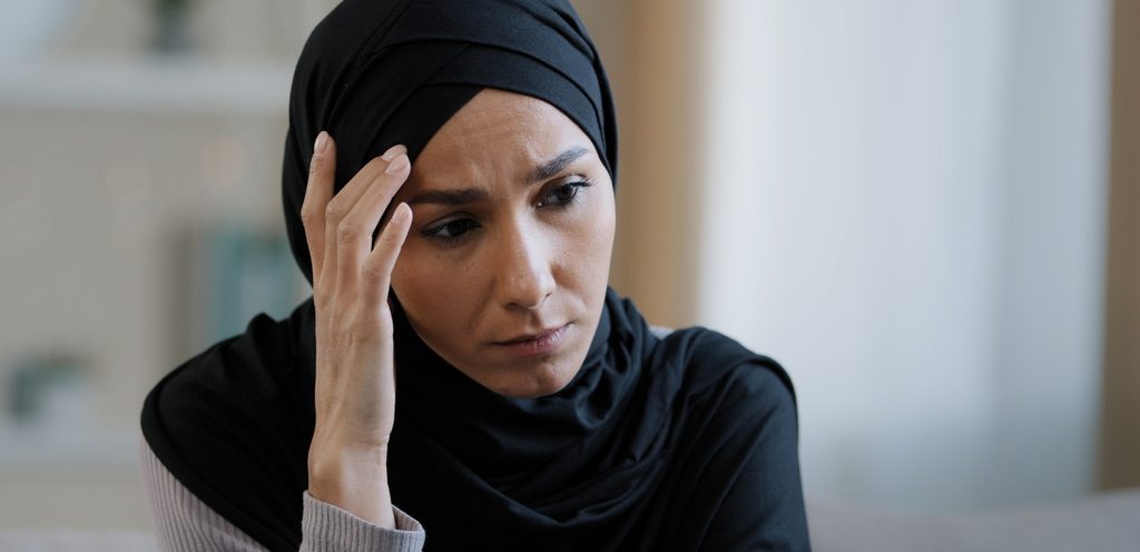 امرأة مسلمة تجلس بحزن وتضع يدها على رأسها
