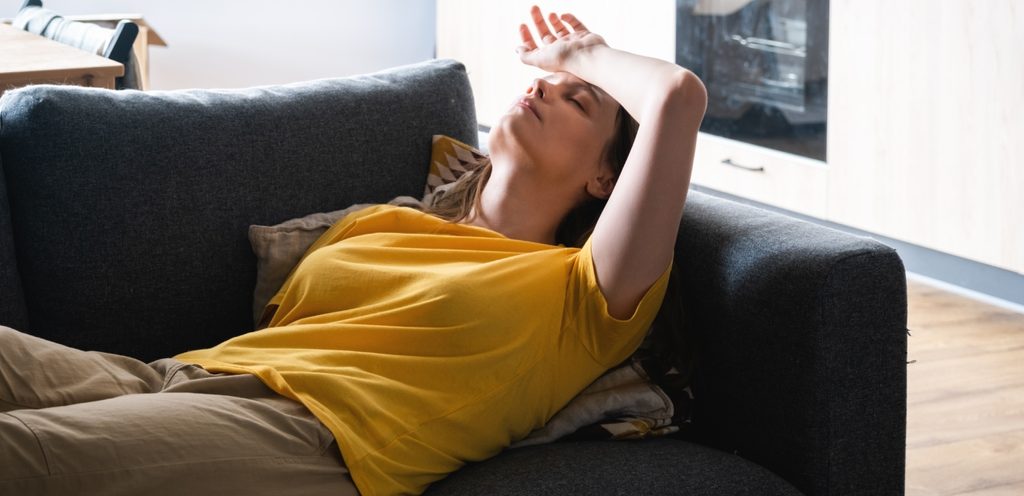 امرأة مستلقية على الكنبة وتضع يدها على رأسها
