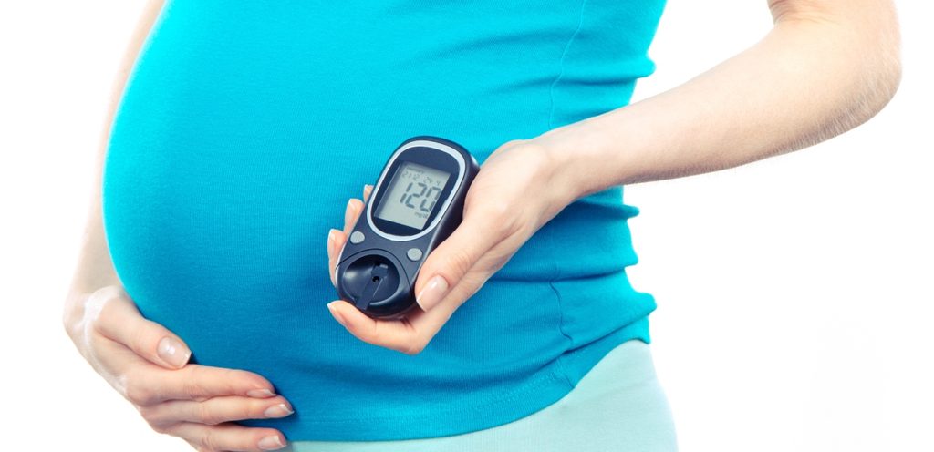 امرأة حامل تضع يدها على بطنها وتمسك باليد الأخرى جهاز قياس السكر