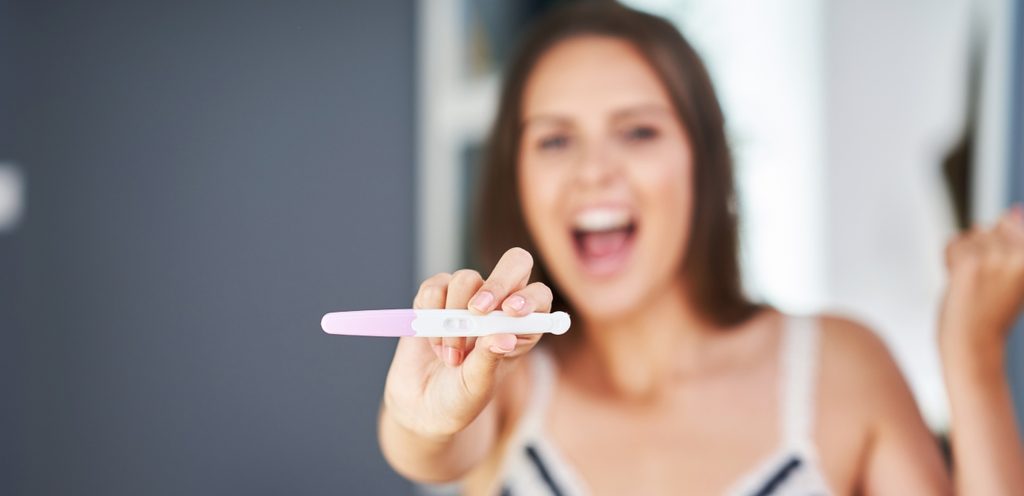 امرأة تُظهر اختبار حملها إلى الأمام بفرح وسعادة