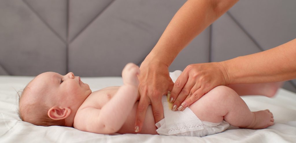 طفل رضيع على السرير ووالدته تغير حفاضه