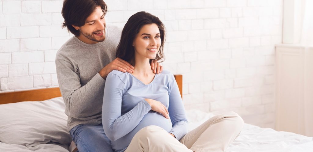 زوج يجلس خلف زوجته الحامل ويضع يديه على كتفيها