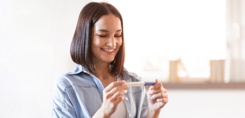 امرأة تمسك اختبار الحمل وتنظر إليه بسعادة