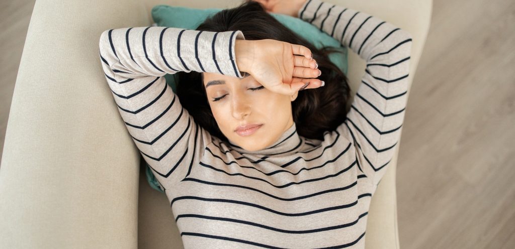 امرأة مستلقية على ظهرها على الكنبة وتضع يدها على رأسها