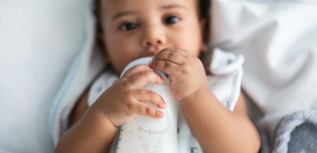 طفل رضيع يشرب الحليب بزجاجة يحملها