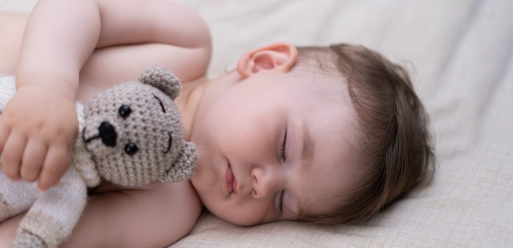 طفل رضيع نائم على السرير وبيده دميته