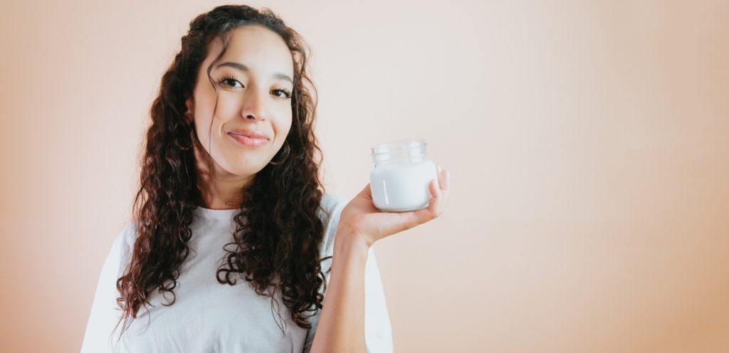 شابّة مبتسمة تمسك مرطبان يحتوي كريم