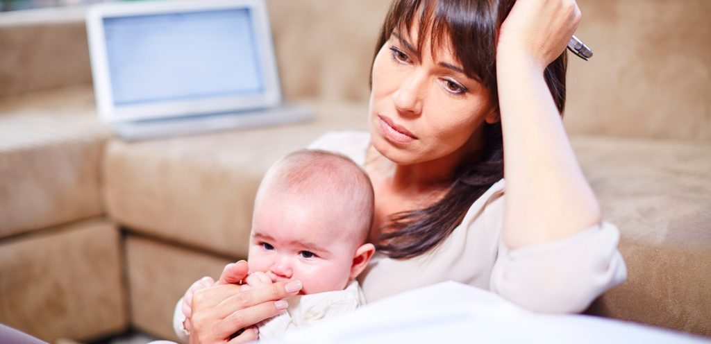 امرأة حزينة تضع يدها على رأسها وتُمسك رضيعها