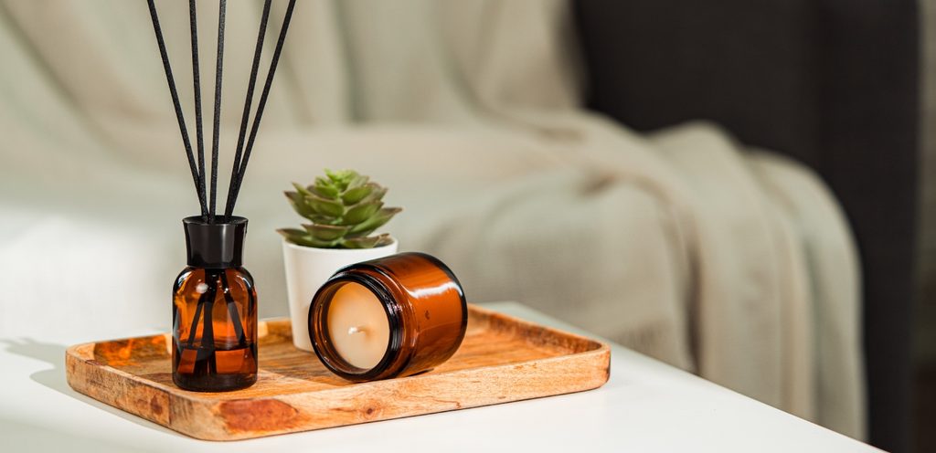 عيدان بخّور في زجاجة بنيّة وبجانبها شمعة ونبتة صغيرة